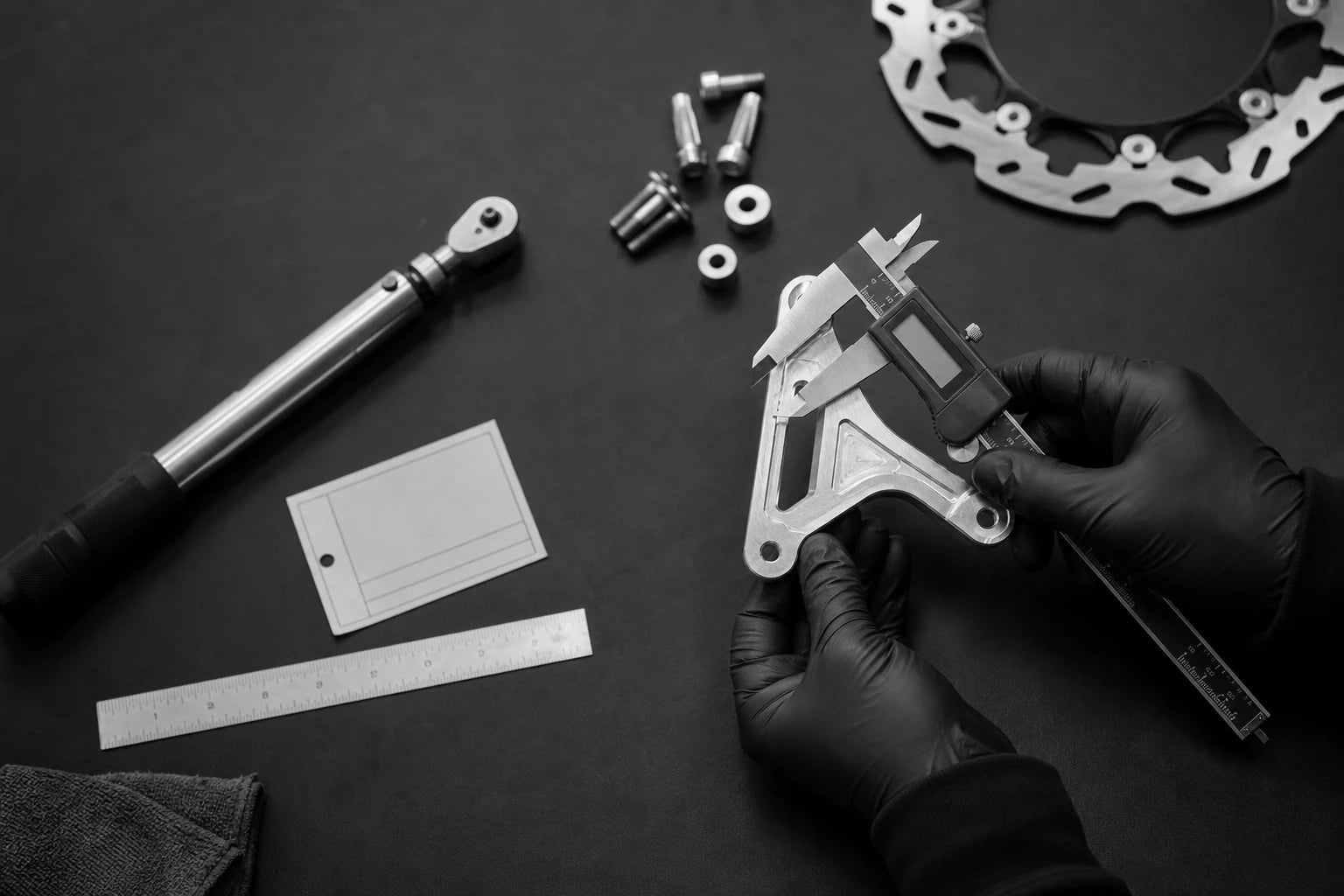 Technician measuring an unbranded machined brake bracket at a workbench